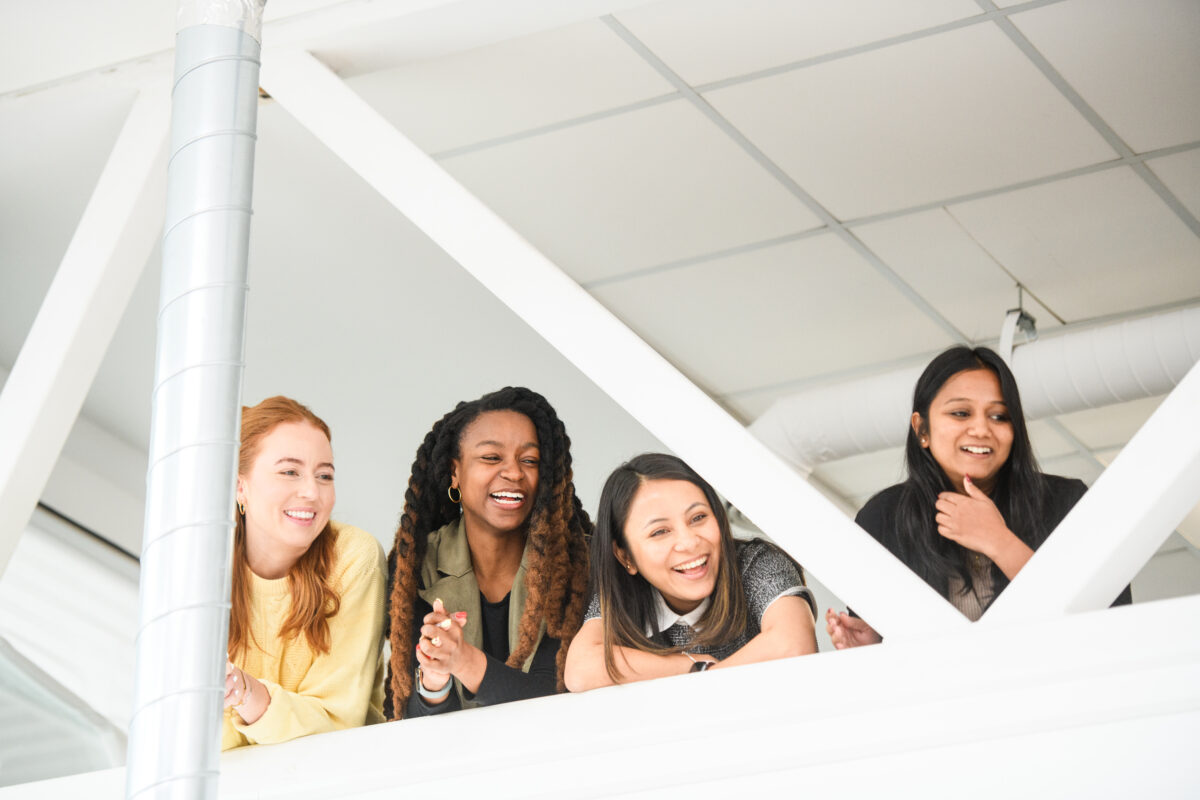 picture in the background is of four women leaning over a railing watching something below and smiling.