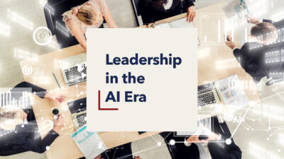 Overhead view of people working at a table with laptops and documents, overlaid with the text “Leadership in the AI Era.”
