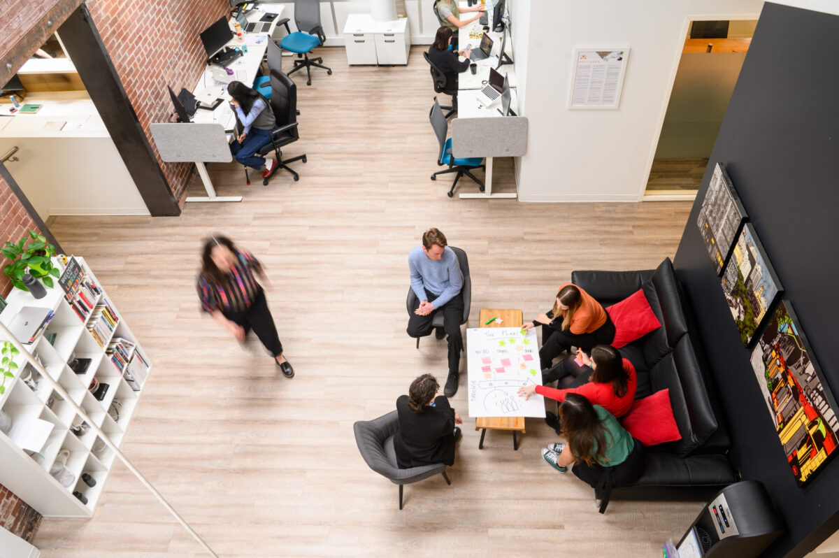 View of a modern office with people working at desks and a collaborative meeting at a sofa.