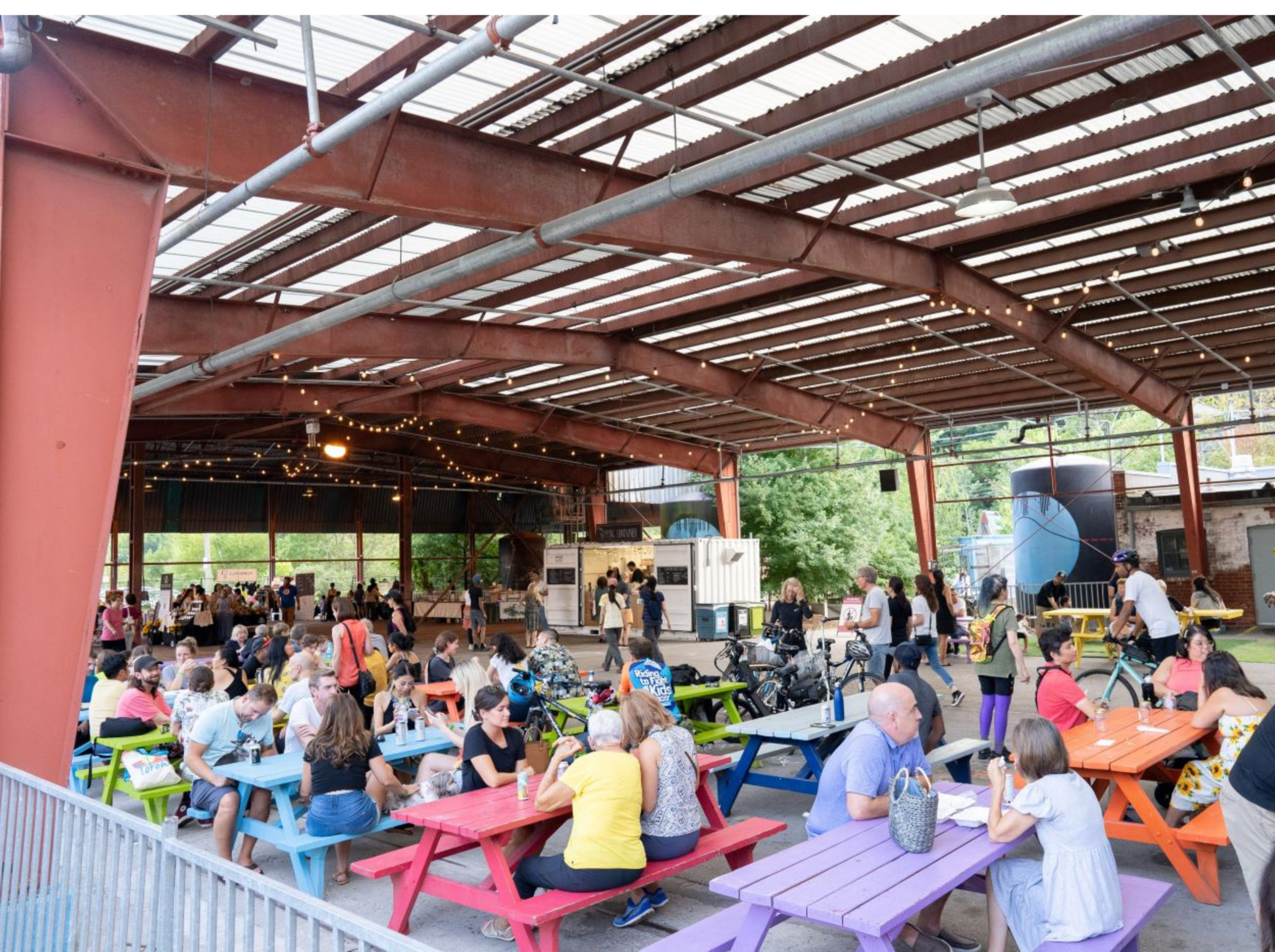 A crowd of happy people sitting at colourful picnic tables at Evergreen Brickworks.