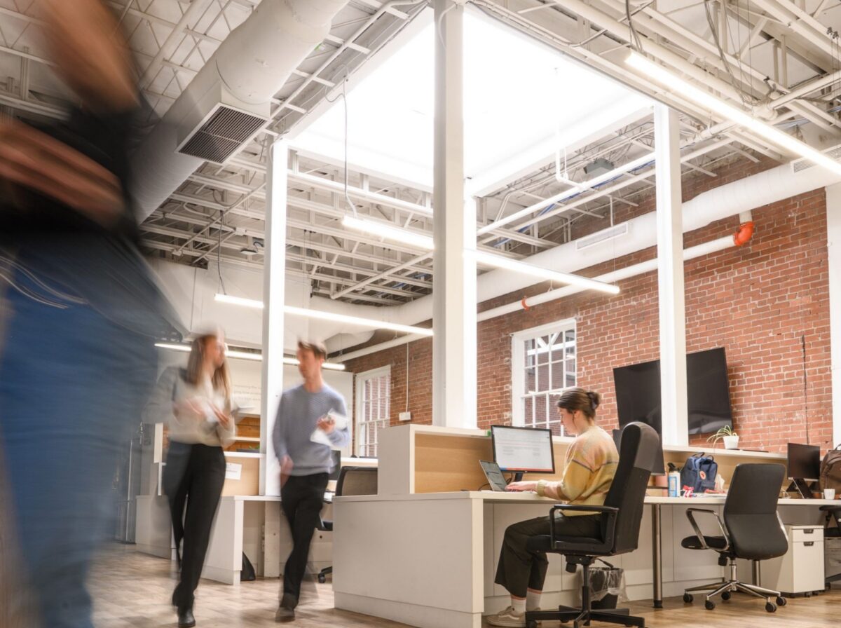 People working and moving through Davis Pier's bright, open-concept office with exposed brick walls.